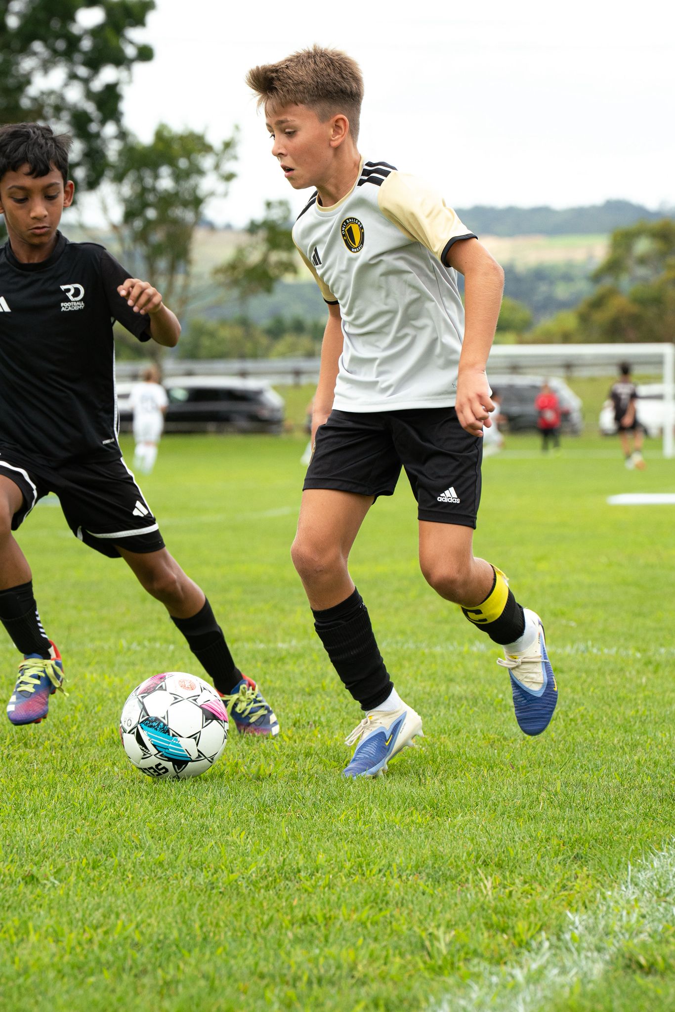 Only Ballers player dribbling past defender in white and gold kit